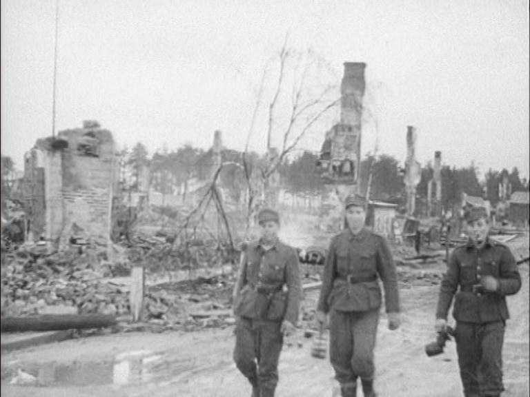 Tre soldater i uniform framför rykande ruiner i finska Rovaniemi, november 1944.