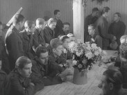 Ett tjugotal hungerstrejkande balter i en barack på Ränneslätt utanför Eksjö 1945, blommor i en vas på ett bord.