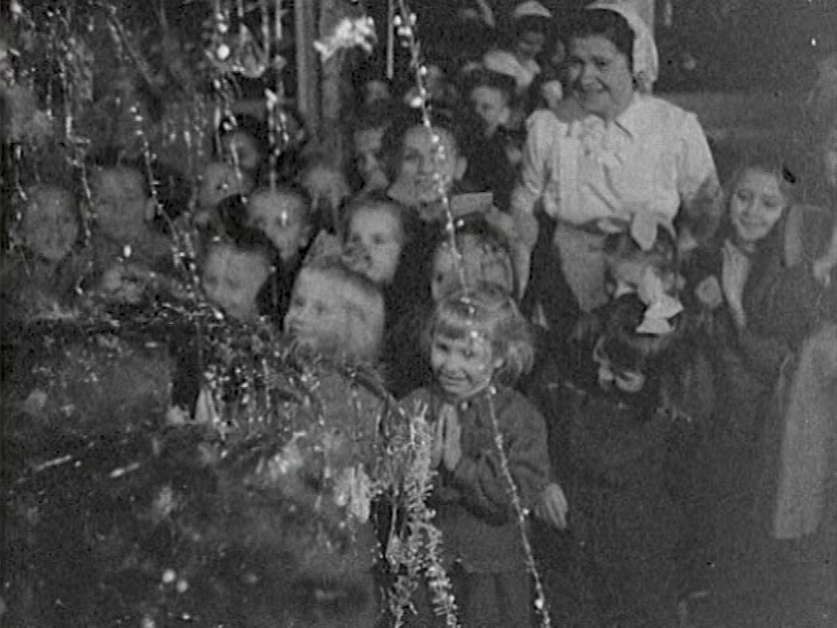 Barn på ett barnhem i Tjeckoslovakien samlas kring en julgran och tittar på brinnande tomtebloss.