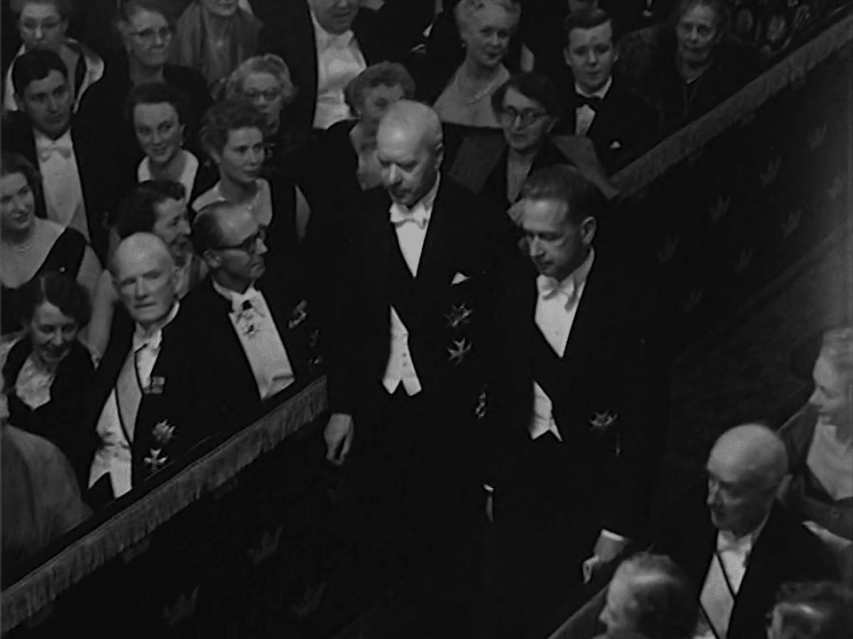 Delar av Svenska Akademin 1954 tågar in i Börssalen. Prominenta gäster sitter i raderna.