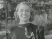Halvbild av en leende Ingrid Bergman i aftonklänning, träd i bakgrunden.
