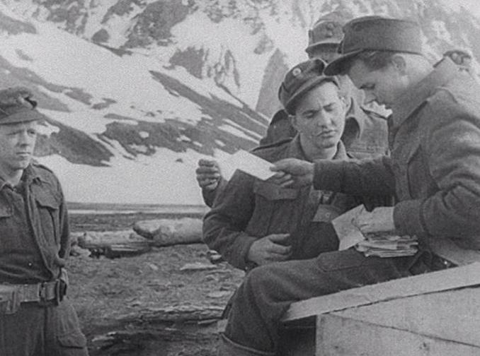 Uniformsklädd man delar ut brev till andra soldater, snöklädd bergssluttning i bakgrunden.