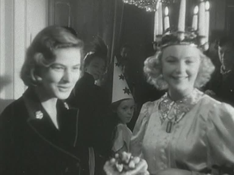 Ingrid Bergman bredvid en leende blond lucia, barn med stjärngossestrut i bakgrunden.