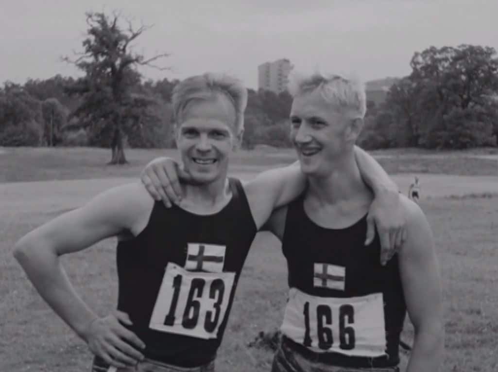 Två finska friidrottare med armarna kring varandras axlar, höghus i bakgrunden.