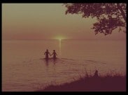 Ett badande par håller varandra i handen, solnedgång i bakgrunden.