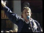 Olof Palme bakom en mikrofon utomhus, han håller höger arm uppsträckt i en gest.