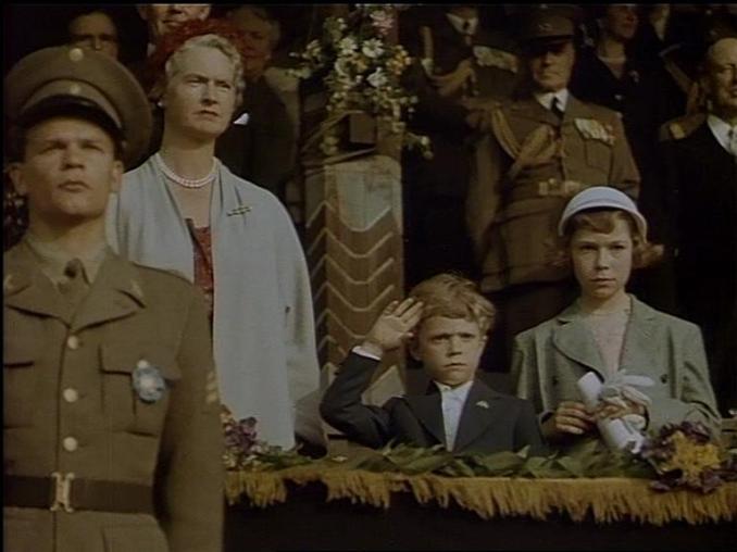 På en läktare står den sjuårige blivande kungen Carl Gustaf och gör honnör mellan Christina och Sibylla.