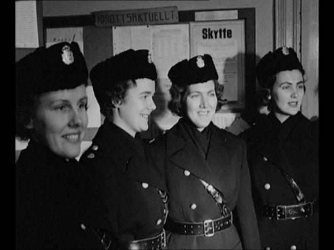 Fyra kvinnliga poliser i uniform framför en anslagstavla.