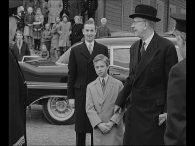 Gustaf VI Adolf och en ung kronprins Carl Gustaf, bil och människor i bakgrunden.